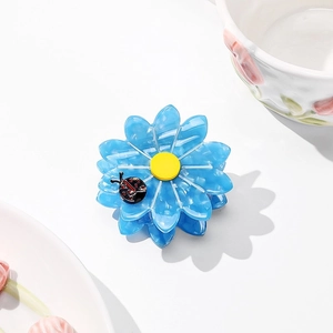 Detail of blue daisy acetate hair claw clip with yellow center and ladybug accent
