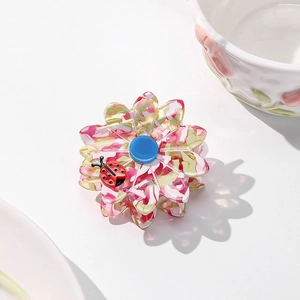 Detailed macro of a floral acetate hair claw with a ladybug accent on a white table