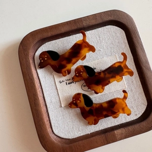 Three tortoise shell dachshund hair clips on a wooden tray with linen background