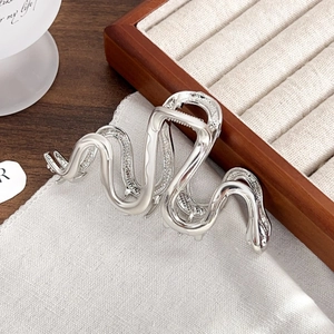 Close-up of a silver wavy metal claw clip with a polished mirror finish on gray fabric