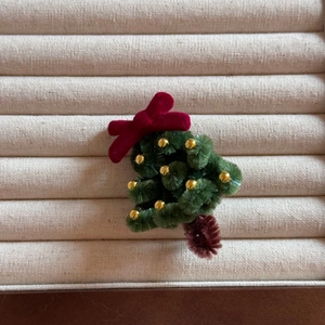 Gros plan d'une pince à cheveux sapin de Noël en peluche avec perles d'or et nœud rouge