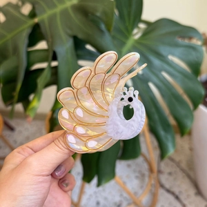 Detailed close-up of a peacock-shaped acetate hair claw with gold accents and sparkling crystals