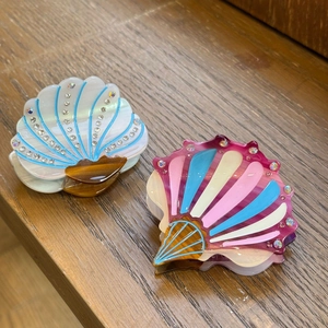 Detail view of shell-shaped acetate hair claws with rhinestones on dark wood background