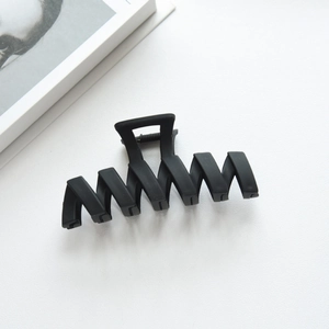 Macro shot of matte black wavy claw clip on white surface with lifestyle accents