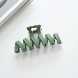 Macro view showing the matte dark green wavy hair claw clip with a strong metal spring