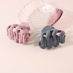 Grandes pinces à cheveux pieuvre au fini mat rose et gris foncé sur un plat décoratif