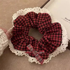 Close-up of red and black plaid scrunchie with white lace trim and bow on light background