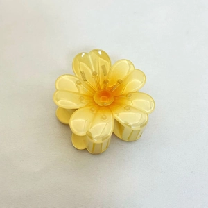 Vue détaillée de dessus d'une pince à cheveux fleur de frangipanier jaune sur tissu blanc
