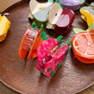 Detailed close-up of fruit-shaped hair clips in various colors on a wooden tray