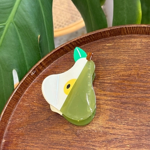 Detail of pear-shaped acetate hair claw clip with leaf accent on a wooden tray