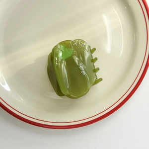 Détail d'une pince à cheveux en acétate vert en forme de poivron avec strass sur assiette
