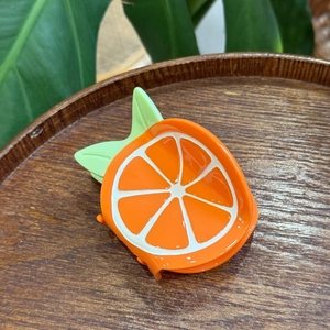 Detail view of a vibrant orange fruit-shaped hair claw clip on a dark wood tray