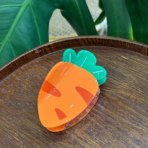Vibrant carrot shaped hair claw clip in orange acrylic on a rustic wooden tray