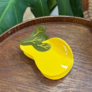 Detailed top view of a bright yellow fruit-shaped hair claw clip with green leaf design