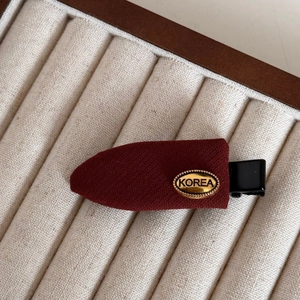 Detail of red fabric hair clip with a gold metal tag and embossed Korea lettering