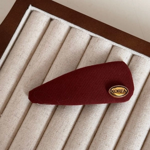 Macro shot of a red fabric hair claw with a gold metal Korea emblem on a velvet tray
