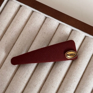 Close-up of a burgundy fabric hair clip with a gold Korea embossed metallic label