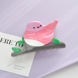 Close-up of bird-shaped acetate hair claw clip with pink and white colors on a branch
