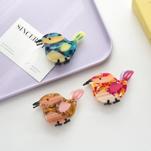 Detailed view of three bird-shaped hair claws made of marble-textured acetate on a tray