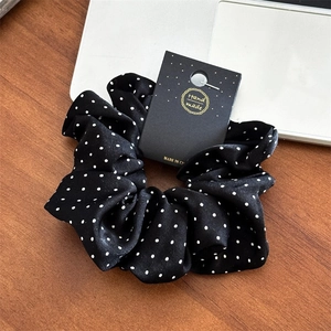 Gros plan d'un chouchou en satin noir à pois sur une carte de présentation sur table en bois
