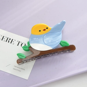 Detailed view of the colorful acetate bird hair claw clip with green leaves on branch