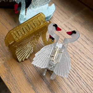 Dettaglio delle mollette per capelli a cigno scintillanti in oro e blu con finitura glitter