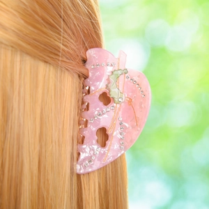 Pink leaf-shaped acetate hair claw with rhinestones on blonde hair with bokeh background