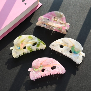 Detailed view of hair claw clips with rhinestones and butterfly patterns in four colors