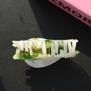 Detail of green marble acetate hair claw clip with rhinestones on a dark surface
