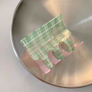Close-up of a green checkered hair claw clip with pink teeth on a metal plate