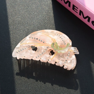 Detailed macro view of pink marble acetate hair claw clip with rhinestones and insect motif