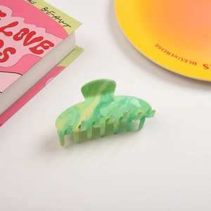 Détail d'une grande pince à cheveux marbrée verte sur un livre rose élégant