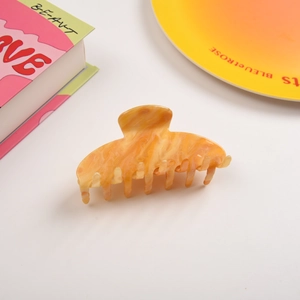 Détail d'une pince à cheveux motif ambre orange avec finition brillante sur fond blanc