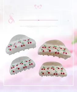 Close-up of four cream-colored hair claws with cute red cherry patterns in a flat lay view