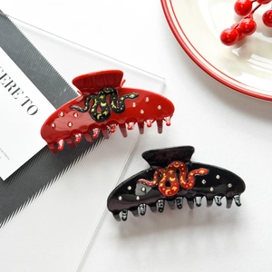 Detail view of red and black snake-shaped acetate hair claws with sparkling rhinestones