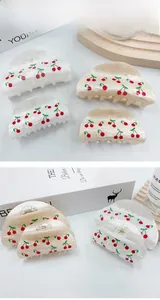 Detail of cherry print hair claws in pearl white and beige finishes on a wooden tray