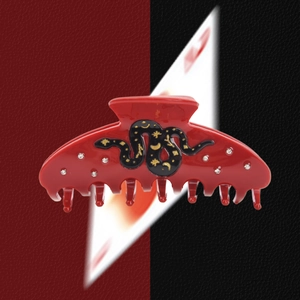 Macro detail of red acetate hair claw featuring a black snake motif with gold celestial icons