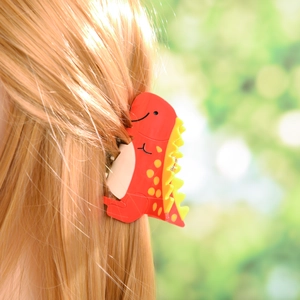 Détail d'une pince à cheveux dinosaure rouge mignonne avec nageoires jaunes sur cheveux