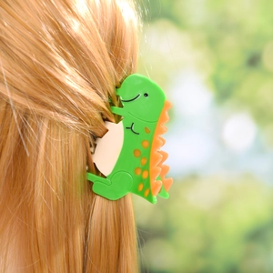 Gros plan d'une pince à cheveux dinosaure verte stylisée sur de longs cheveux blonds