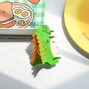 Detalle de una linda pinza para el cabello de dinosaurio verde con detalles naranjas