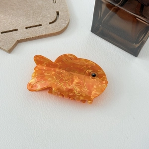 Détail d'une pince à cheveux en forme de poisson en acétate orange avec écailles dorées