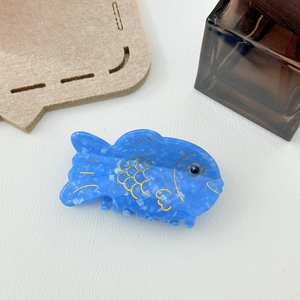 Gros plan sur une pince à cheveux poisson en acétate bleu avec écailles dorées
