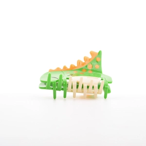 Détail d'une jolie pince à cheveux dinosaure verte avec des détails dentelés orange