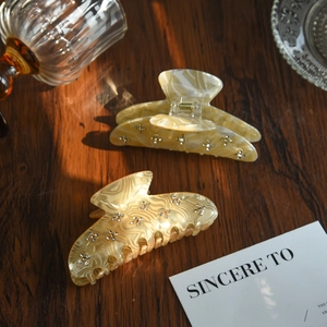 Detail of marble pattern acetate hair claws with rhinestones on dark wood surface
