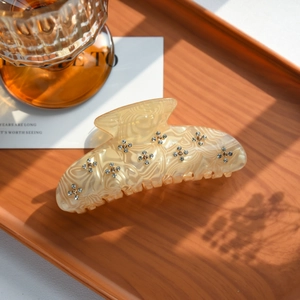 Detailed view of a cream acetate hair claw clip with sparkling rhinestone flower patterns
