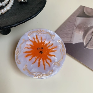 Detail view of round acetate hair claw clip featuring a purple marble finish and sun face design