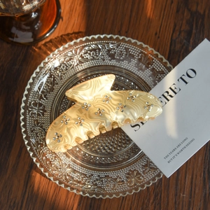 Detail of a beige marble acetate hair claw clip with crystal flower accents on a plate