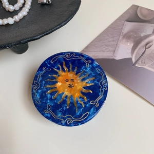 Detail of sun-shaped acetate hair claw with blue marble pattern and gold line accents