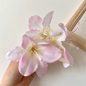 Close-up of pink and white lily hair claw clip with a clear base and gold spring detail