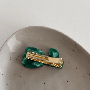 Close-up of a dark green acetate tulip hair clip with marble texture on a ceramic plate